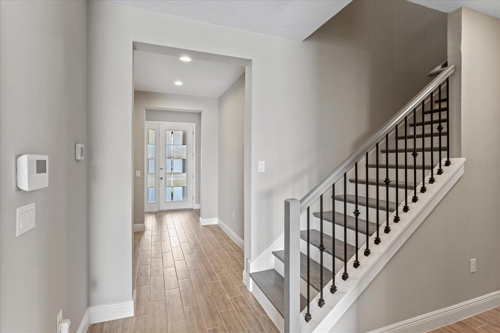 A foyer features wood-look tile flooring, a staircase with black metal railings, and a front door — 17314 WILD DAISY DRIVE, WINTER GARDEN, FL