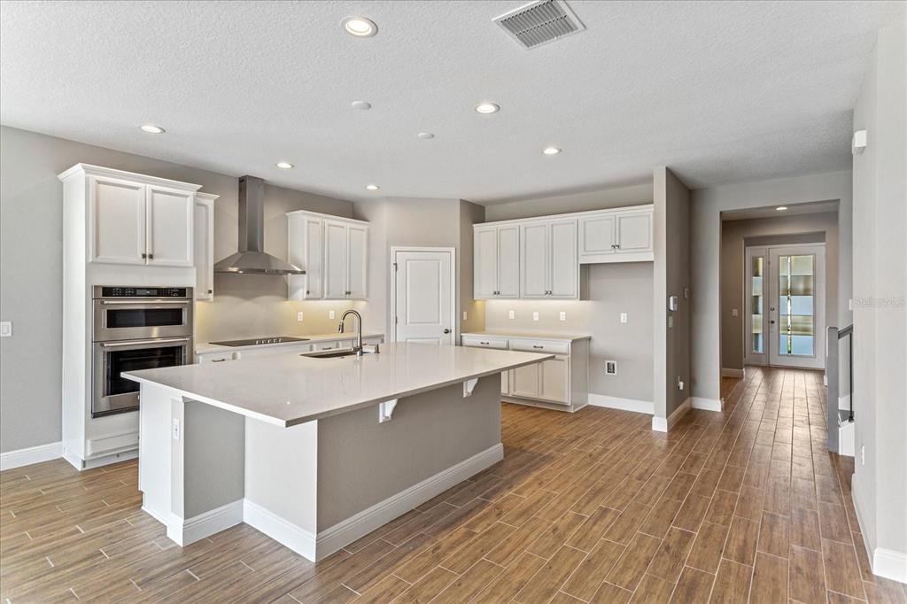 A modern kitchen features white cabinetry, a large island with a sink, and wood-look flooring — 17314 WILD DAISY DRIVE, WINTER GARDEN, FL