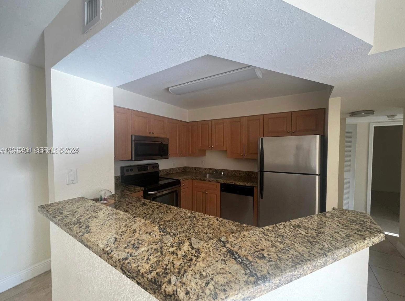 A kitchen features wood cabinets, granite countertops, and stainless steel appliances with a breakfast bar — 5112 NW 79 Ave # 202, Doral FL 33166, DORAL, FL