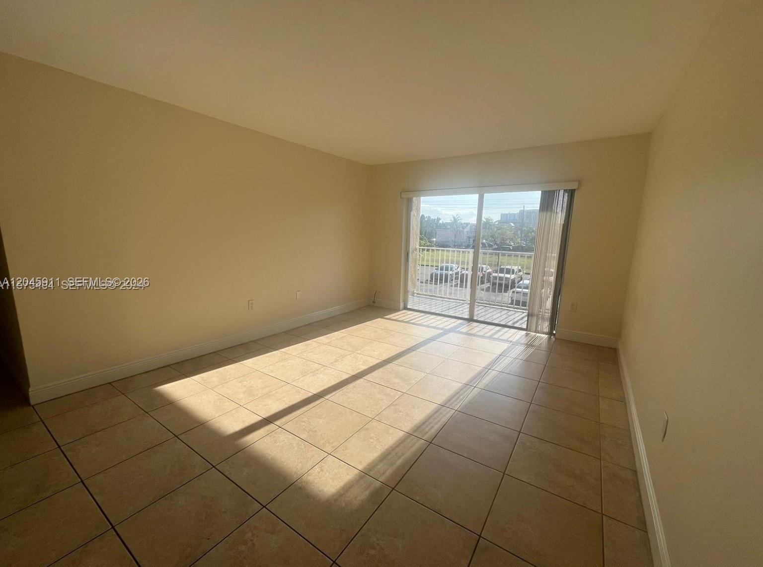 An empty room features beige tile flooring, light-colored walls, and a sliding glass door to a balcony — 5112 NW 79 Ave # 202, Doral FL 33166, DORAL, FL