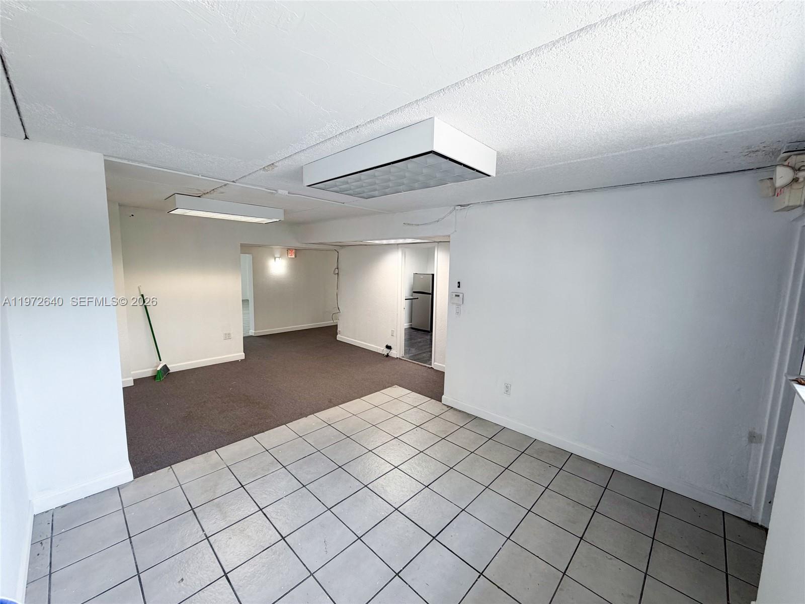 An interior view shows a room with tiled flooring, a carpeted area, and fluorescent lighting — 18500 NE 5th Ave, Miami FL 33179, MIAMI, FL