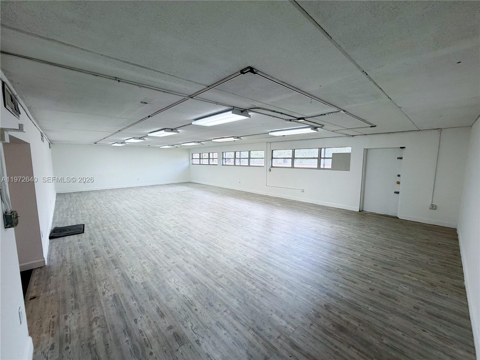 An empty commercial office space features white walls, wood-look flooring, and exposed ceiling lighting — 18500 NE 5th Ave, Miami FL 33179, MIAMI, FL