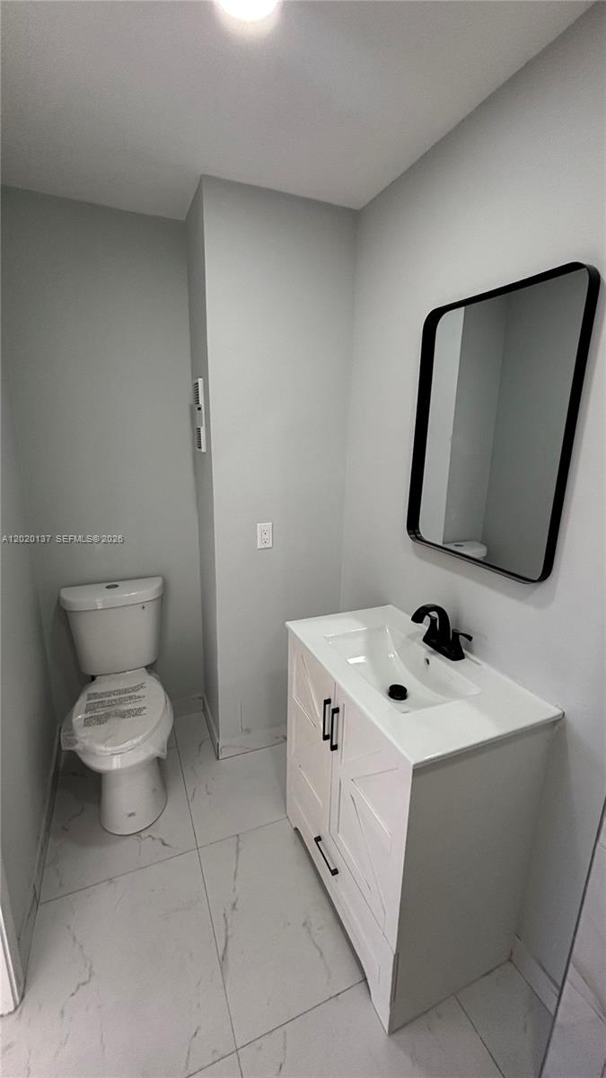 A modern bathroom features a white vanity, a black-framed mirror, and a toilet on tile flooring — 20825 NE 8th Ct # 19, Miami FL 33179, MIAMI, FL