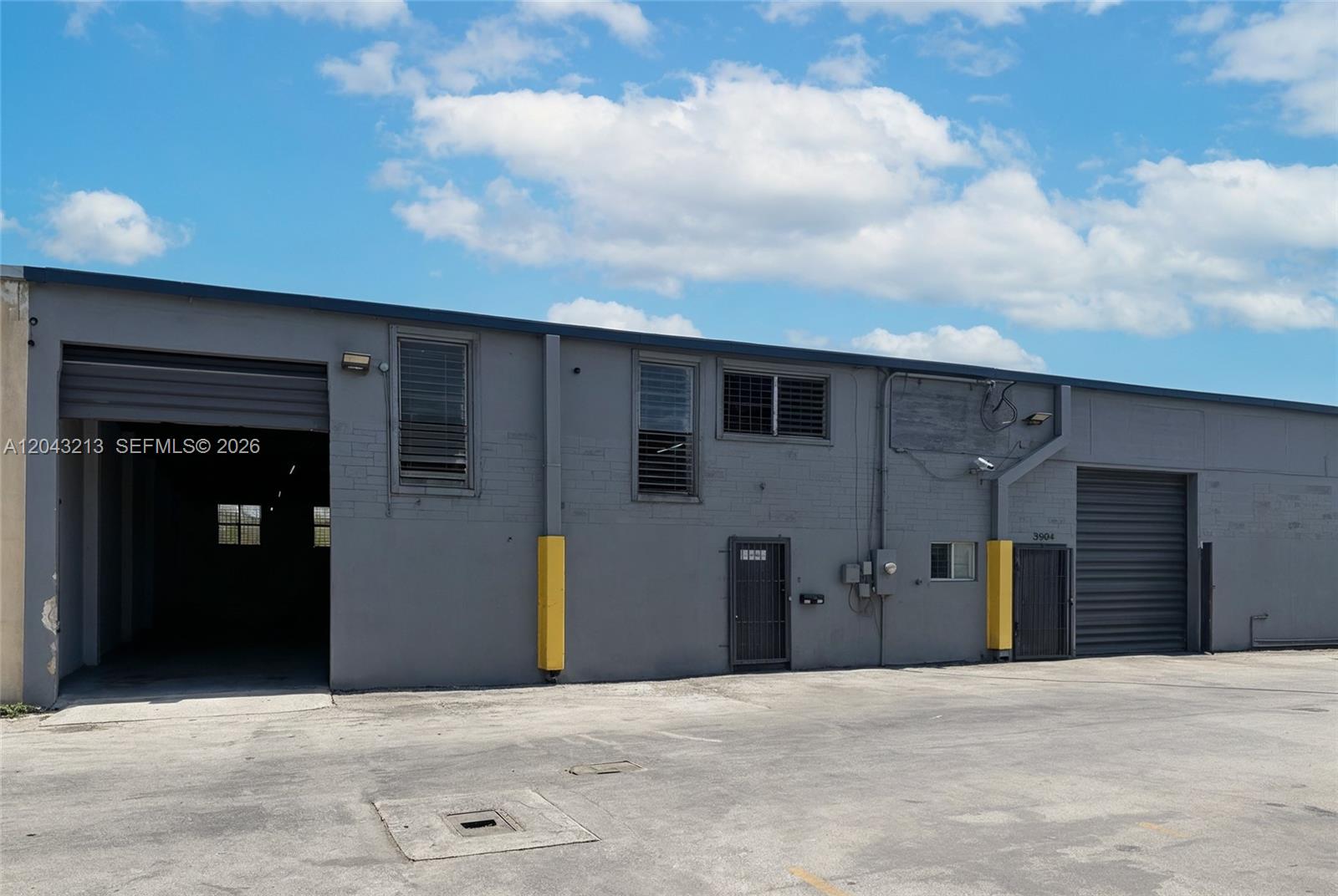 A gray industrial building features two roll-up doors, two pedestrian doors, and yellow protective bollards — 3904 NW 32nd Ave, Miami FL 33142, MIAMI, FL