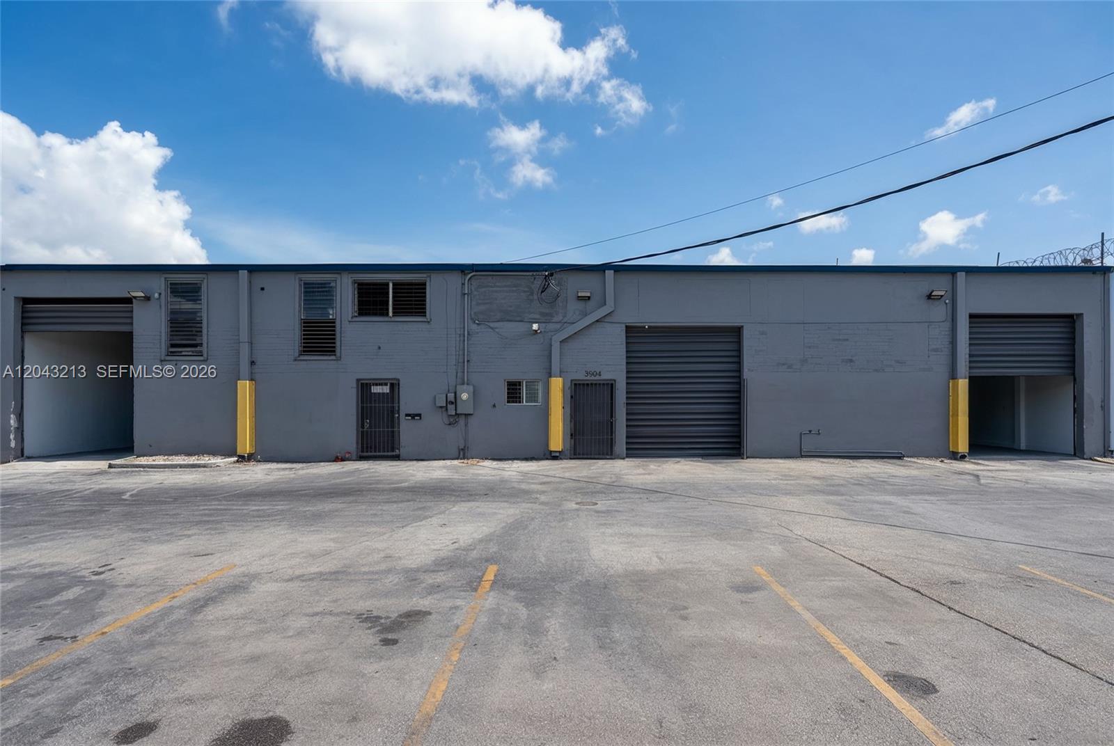 A gray industrial building features two roll-up doors, two pedestrian doors, and a paved parking lot — 3904 NW 32nd Ave, Miami FL 33142, MIAMI, FL