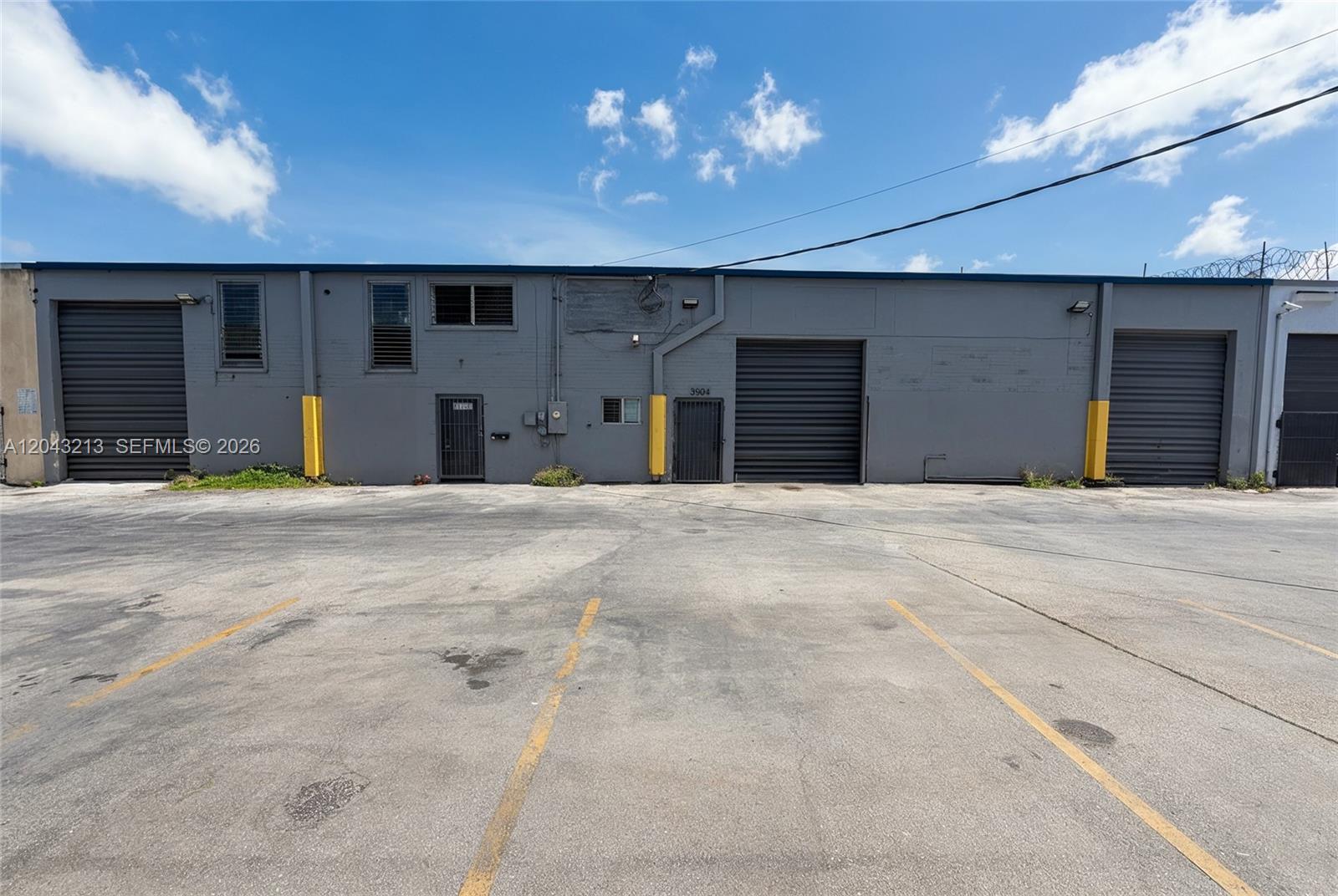 A gray industrial warehouse building features multiple roll-up doors and a paved parking lot — 3904 NW 32nd Ave, Miami FL 33142, MIAMI, FL