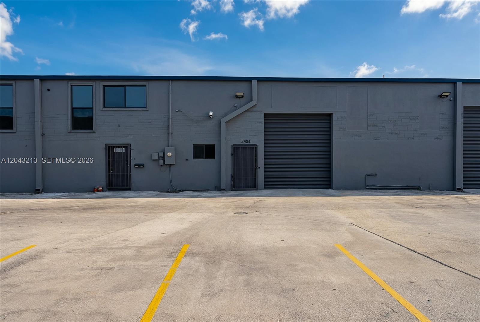 The exterior of a gray industrial warehouse building features a roll-up door and parking spaces — 3904 NW 32nd Ave, Miami FL 33142, MIAMI, FL