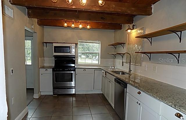 A kitchen features white cabinets, granite countertops, open shelving, and exposed wooden ceiling beams — 2611 223RD STREET E, BRADENTON, FL