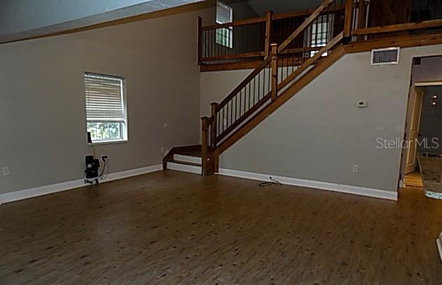A living room with light wood-look flooring, a window, and a wooden staircase to a loft — 2611 223RD STREET E, BRADENTON, FL