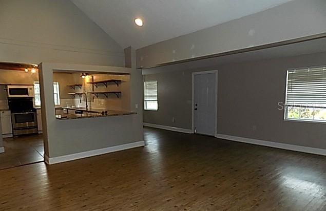 A living area with wood-look flooring, a vaulted ceiling, and an open kitchen pass-through — 2611 223RD STREET E, BRADENTON, FL