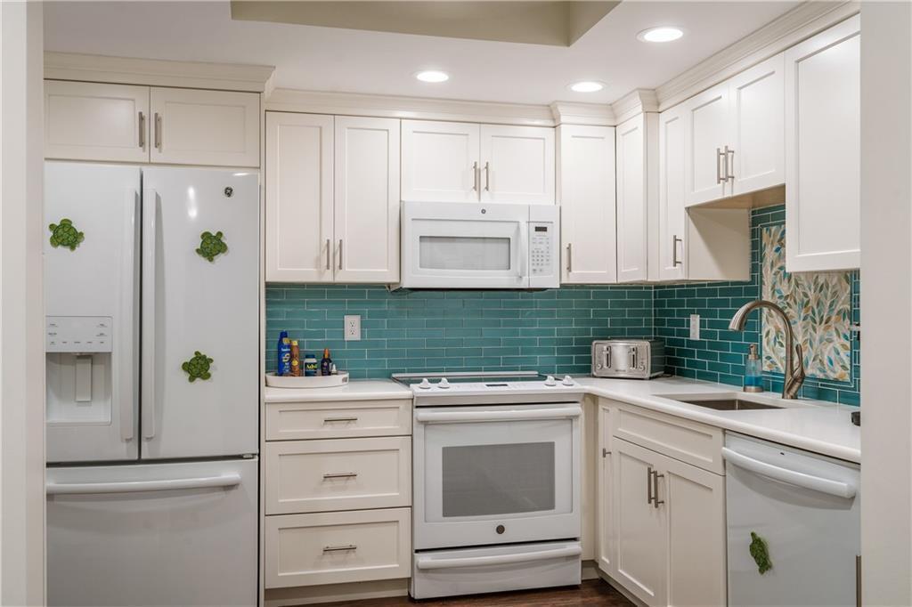 A kitchen with white cabinets, a teal subway tile backsplash, and white appliances — 5601 Highway A1a # 304n, Vero Beach FL 32963, VERO BEACH, FL