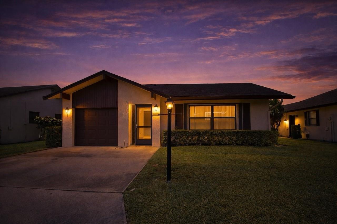 A single-story house with a garage and a lit front entrance at sunset — 3305 Silver Buttonwood Drive, FL 33463, FL