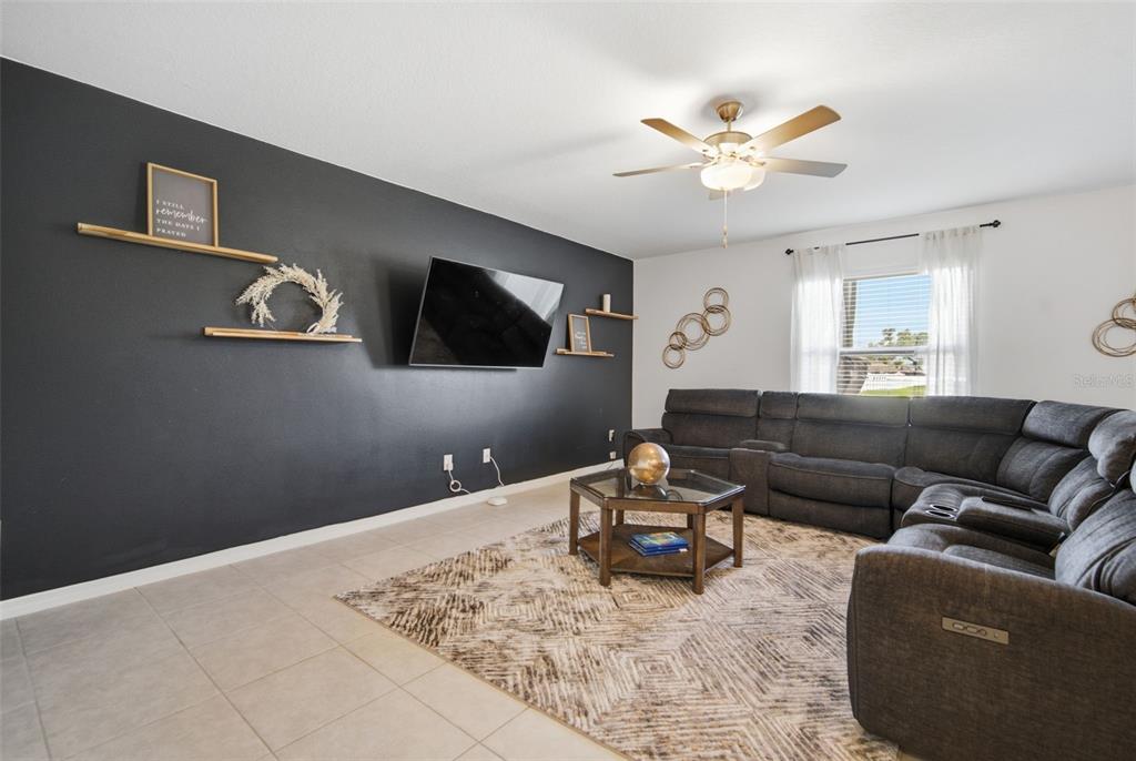 A living room features a dark accent wall with a mounted television and floating shelves — 6469 BAR S BAR TRAIL, ZEPHYRHILLS, FL