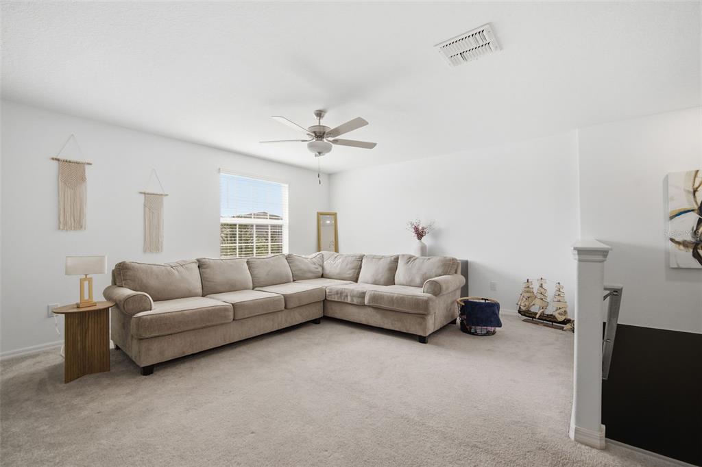 A carpeted living room features a large beige sectional sofa, a ceiling fan, and windows — 6469 BAR S BAR TRAIL, ZEPHYRHILLS, FL