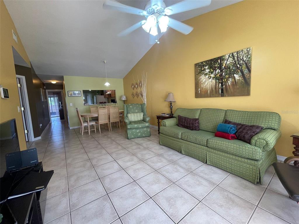 A living room with a green sofa, matching armchair, tiled floors, and a vaulted ceiling — 3004 JON JON COURT, ORLANDO, FL