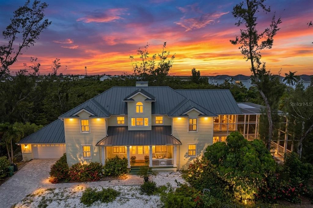 A two-story yellow house with a metal roof stands under a vibrant sunset sky — 793 JUNGLE QUEEN WAY, LONGBOAT KEY, FL