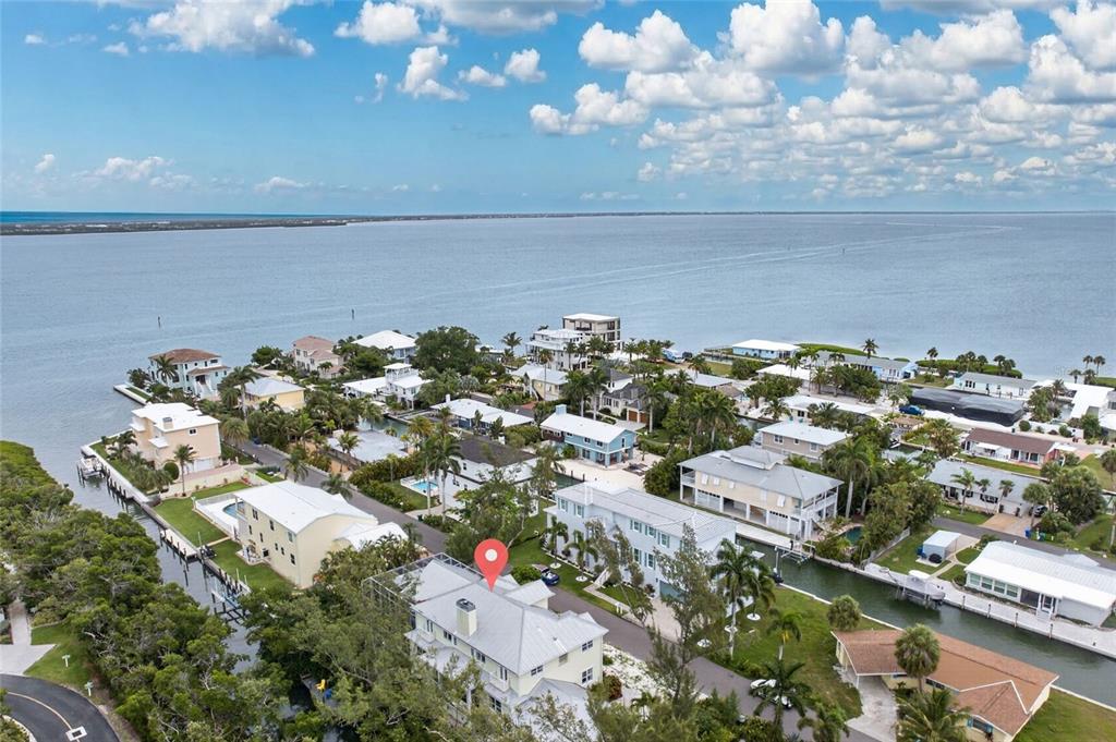 An aerial view shows a coastal neighborhood with houses, canals, and a large body of water — 793 JUNGLE QUEEN WAY, LONGBOAT KEY, FL