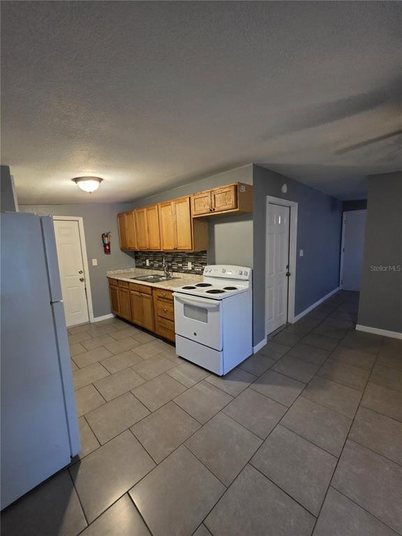 A kitchen features wood cabinets, a white stove, and gray tile flooring — 1328 37TH STREET NW, WINTER HAVEN, FL
