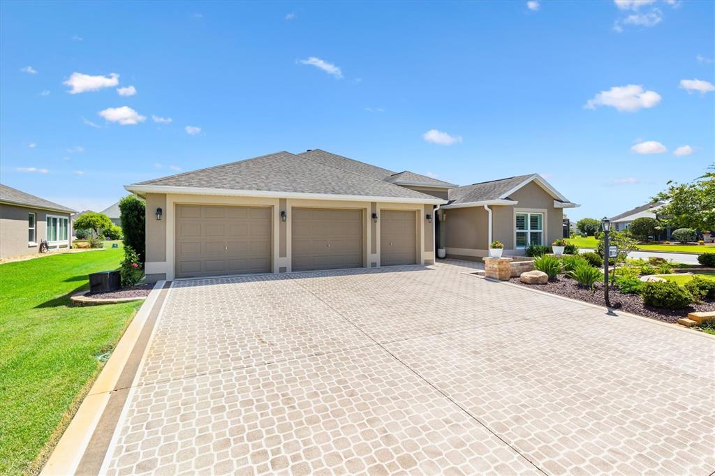 A beige house with a three-car garage and a paved driveway under a blue sky — 728 CONGAREE LOOP, THE VILLAGES, FL