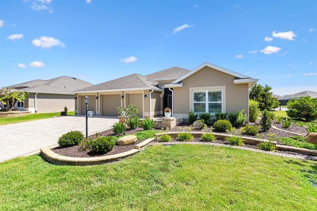 A single-story house with a beige exterior, a three-car garage, and a landscaped front yard — 728 CONGAREE LOOP, THE VILLAGES, FL