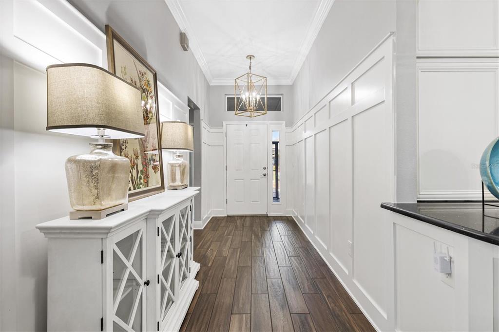 A bright entryway features white board-and-batten walls, wood-look tile flooring, and a geometric pendant light — 728 CONGAREE LOOP, THE VILLAGES, FL