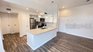 A kitchen with white cabinets, granite countertops, and stainless steel appliances opens to a living area — 7270 WESTPOINTE BOULEVARD UNIT 933, ORLANDO, FL
