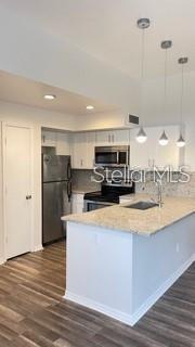 A kitchen features white cabinets, stainless steel appliances, a granite island, and wood-look flooring — 7270 WESTPOINTE BOULEVARD UNIT 933, ORLANDO, FL