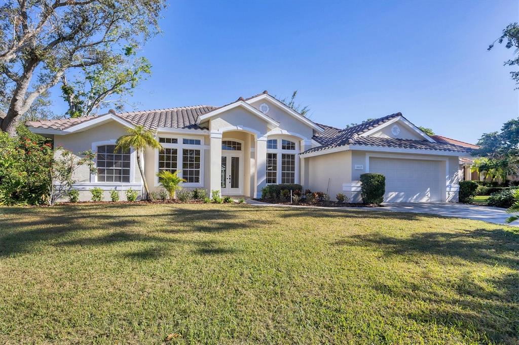 A single-story suburban house with a tile roof, beige stucco exterior, and a two-car garage — 6615 HUNTER COMBE CROSSING, UNIVERSITY PARK, FL