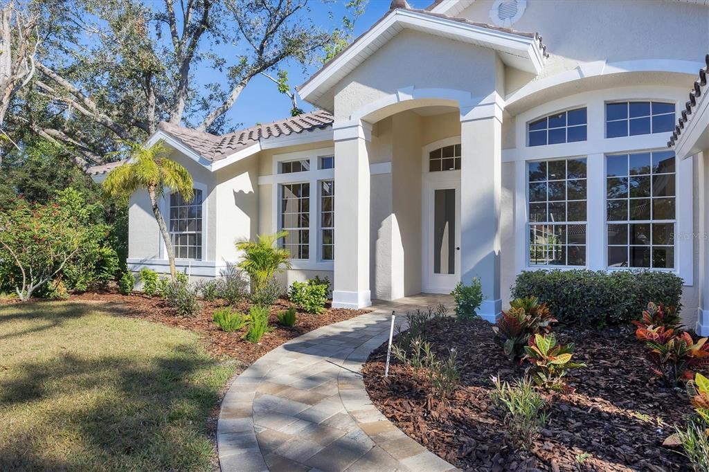 A paved walkway leads to the front entrance of a beige house with large windows — 6615 HUNTER COMBE CROSSING, UNIVERSITY PARK, FL