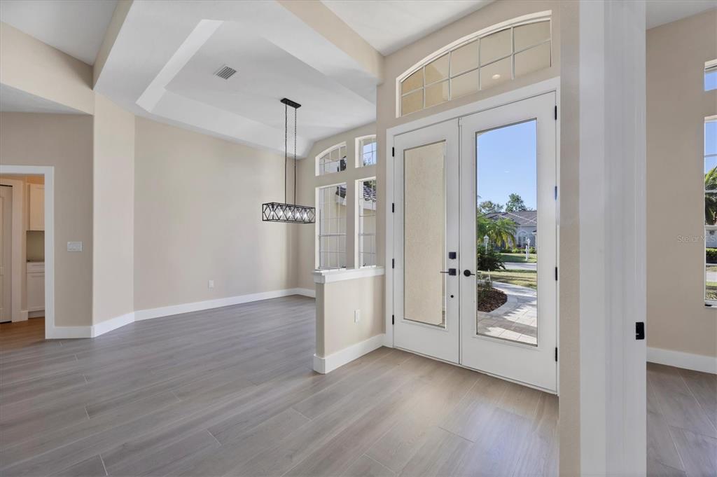 An entryway with light wood-look flooring, a tray ceiling, and double glass-paneled front doors — 6615 HUNTER COMBE CROSSING, UNIVERSITY PARK, FL