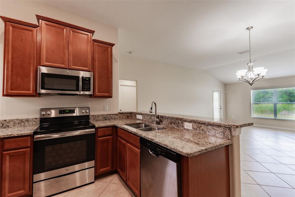 A kitchen features wood cabinets, granite countertops, stainless steel appliances, and tile flooring — 18591 BRIAR OAKS DRIVE, HUDSON, FL