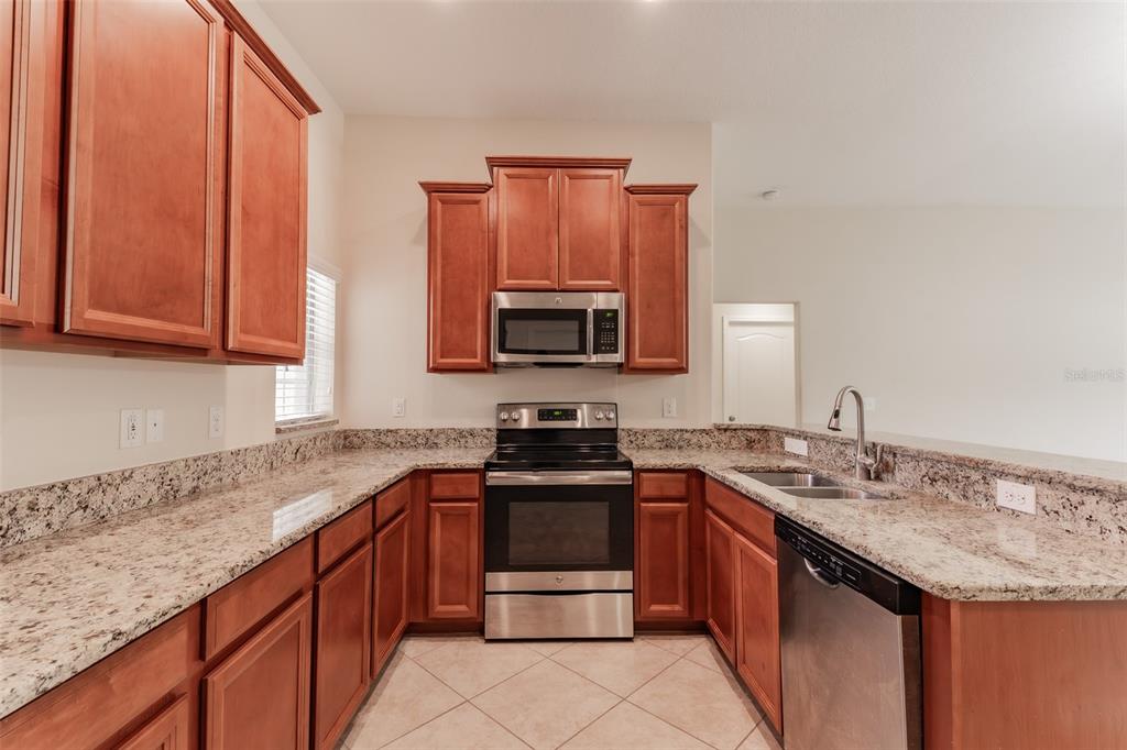 A kitchen features wood cabinets, granite countertops, stainless steel appliances, and tile flooring — 18591 BRIAR OAKS DRIVE, HUDSON, FL