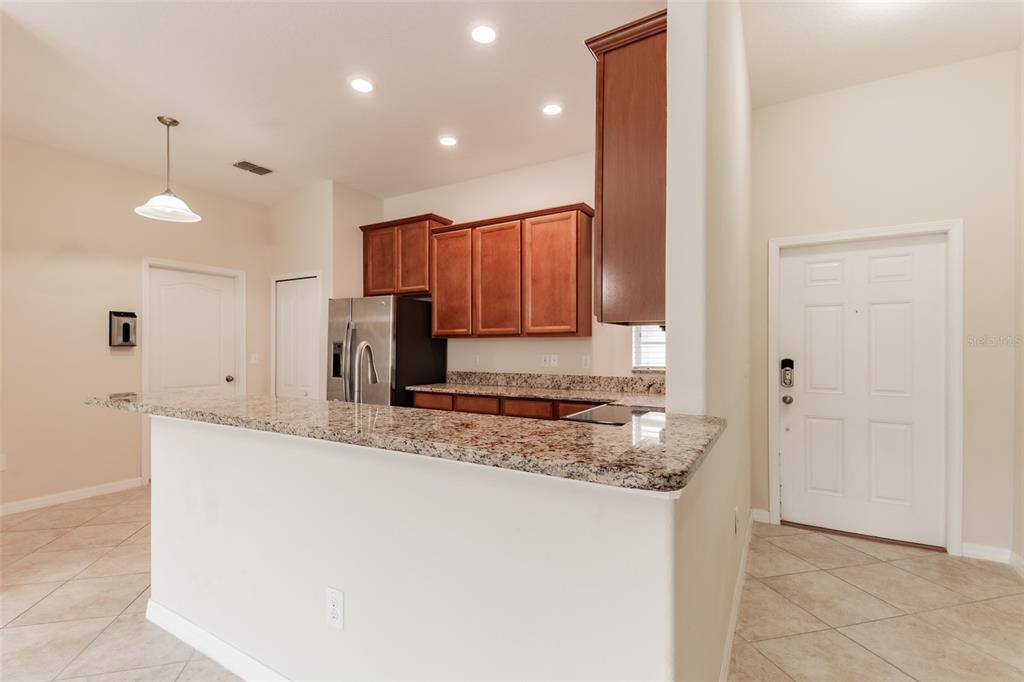 A kitchen with granite countertops, wooden cabinets, and stainless steel appliances overlooks a tiled area — 18591 BRIAR OAKS DRIVE, HUDSON, FL
