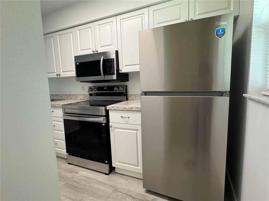 A kitchen features white cabinets, stainless steel appliances, and a speckled countertop — 6428 HAMLET DRIVE UNIT A, ENGLEWOOD, FL