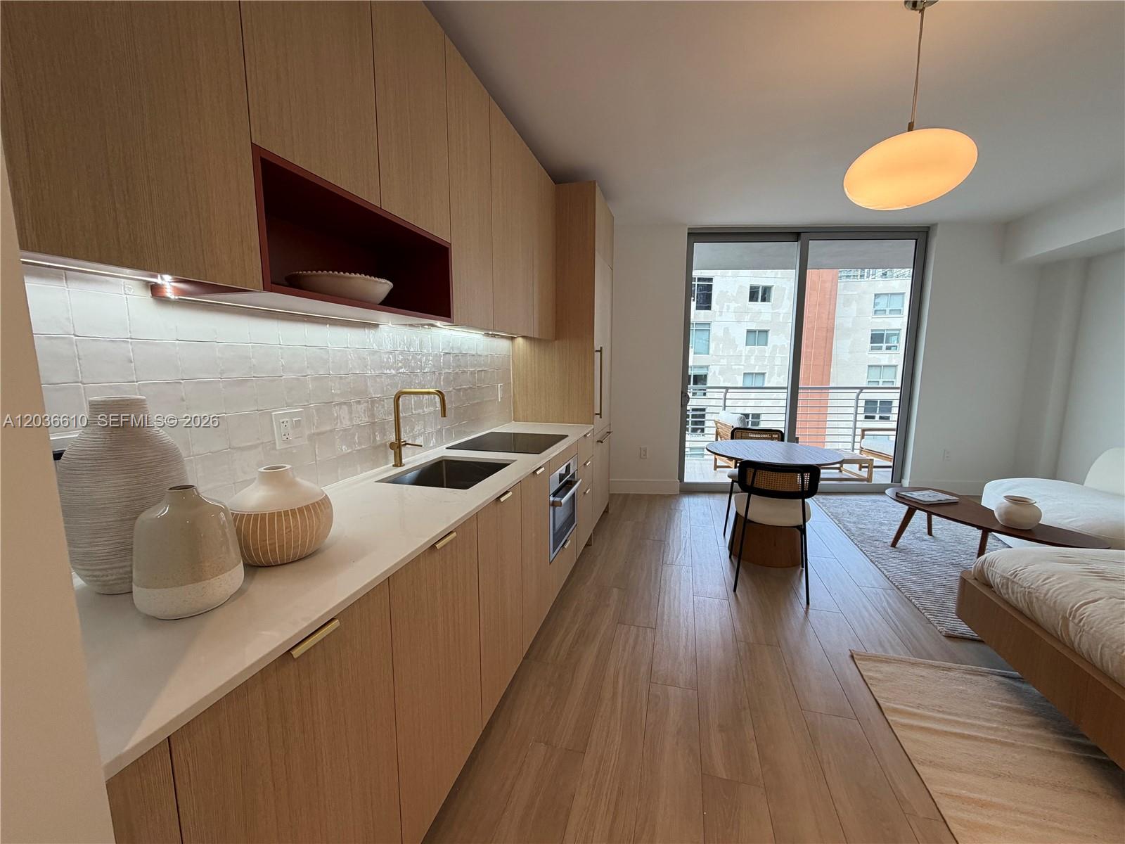 A modern kitchen with light wood cabinets and white tile backsplash opens to a living area — 90 NE 32 # 1014, Miami FL 33149, MIAMI, FL