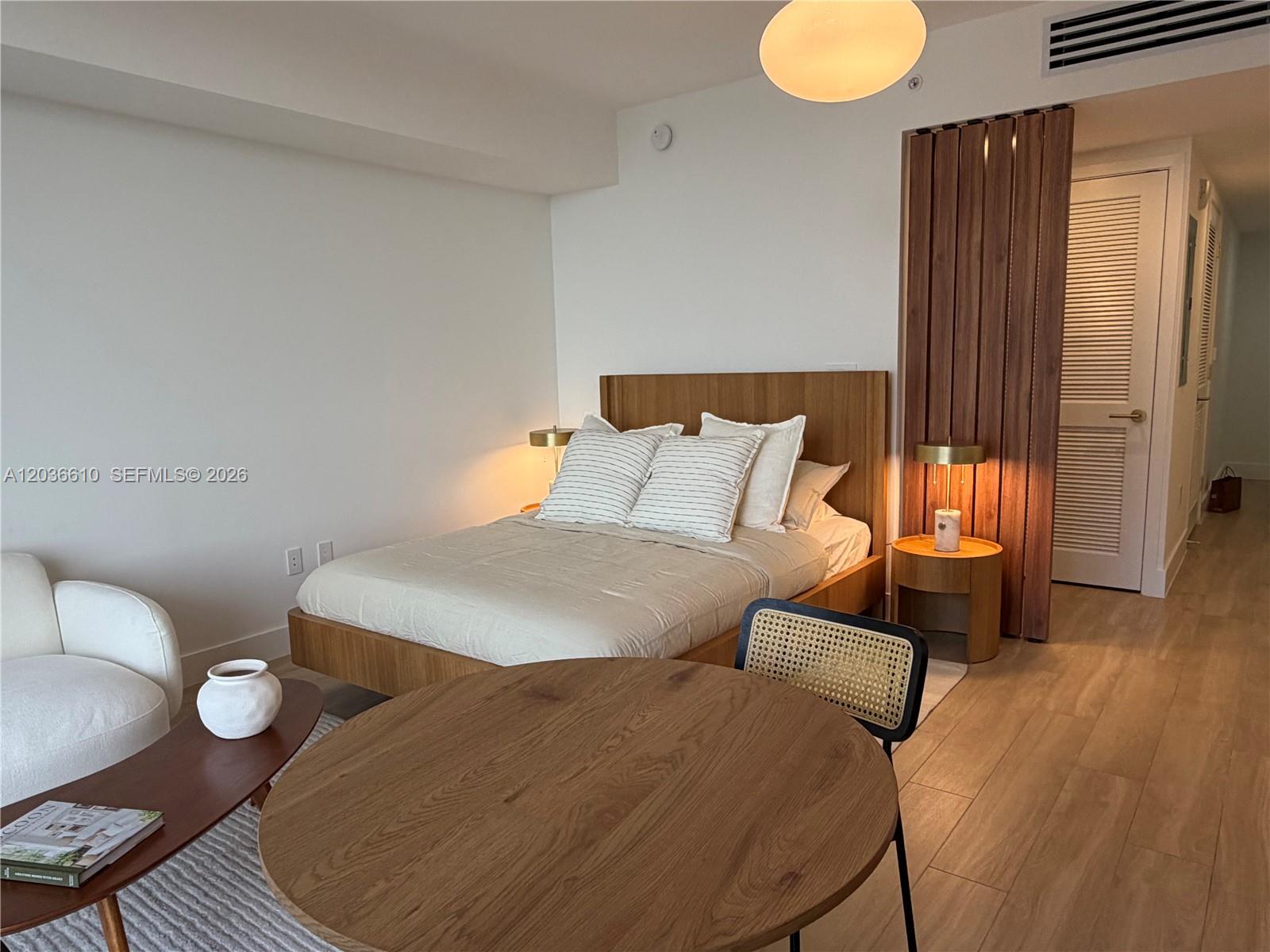 A modern bedroom features a wooden bed frame, round dining table, and slatted wood partition — 90 NE 32 # 1014, Miami FL 33149, MIAMI, FL
