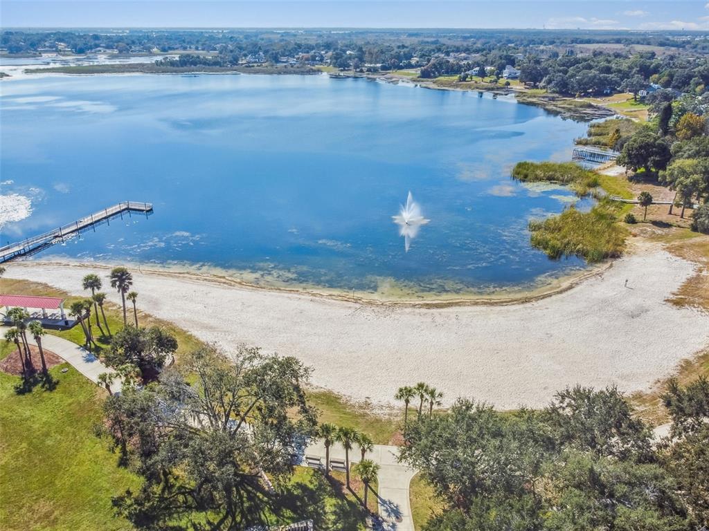 An aerial view shows a sandy beach, a long wooden pier, and a lake fountain — 518 INGLESIDE LANE, HAINES CITY, FL