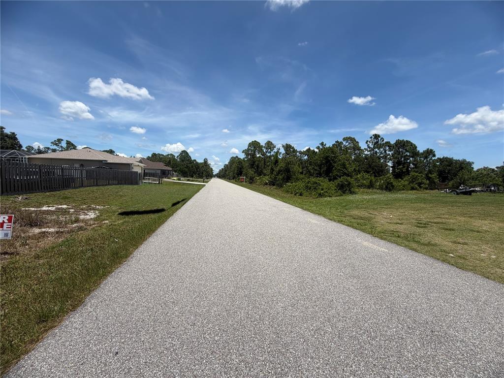 A paved road stretches into the distance between a residential fence and an open lot — 3419 VESSELS ROAD, PORT CHARLOTTE, FL