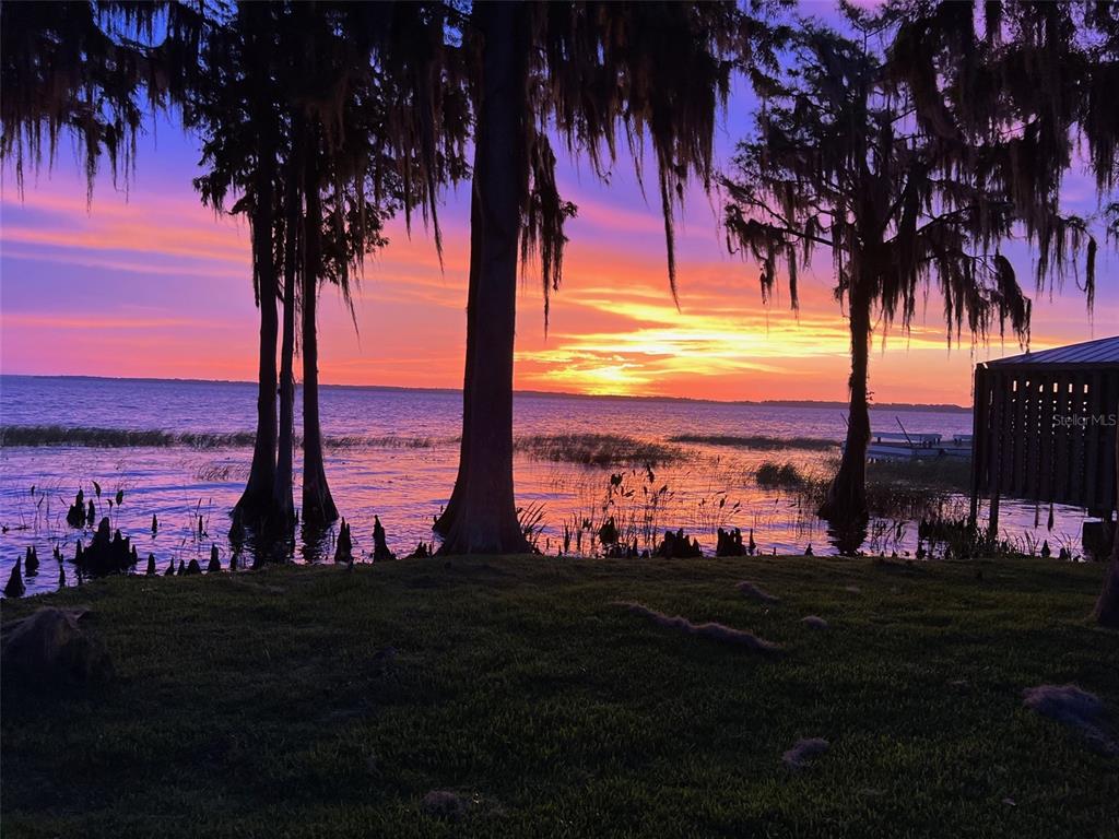 A vibrant sunset glows over a lake with cypress trees and a wooden dock — 11322 DEAD RIVER ROAD, TAVARES, FL