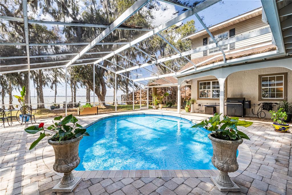A screened-in pool patio features brick pavers, potted plants, and a view of a lake — 11322 DEAD RIVER ROAD, TAVARES, FL