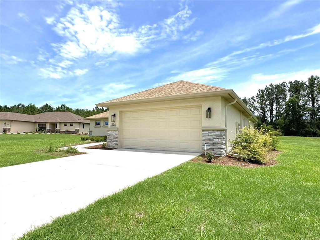 A beige house exterior features a two-car garage with stone accents and a concrete driveway — 1724 E GATE DANCER CIRCLE, INVERNESS, FL