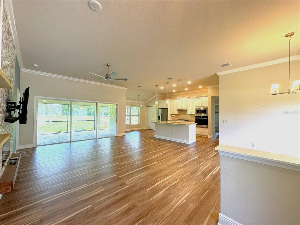 An open-concept living area features wood-look flooring, a kitchen with white cabinets, and sliding doors — 1724 E GATE DANCER CIRCLE, INVERNESS, FL