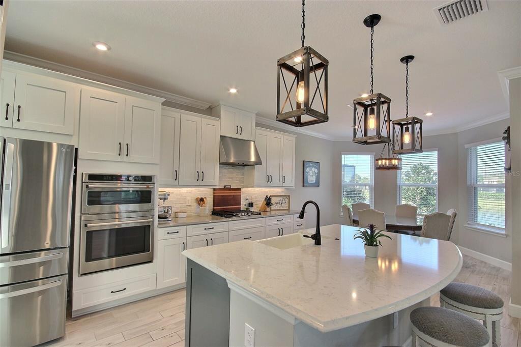 A modern kitchen features white cabinets, stainless steel appliances, a large island, and pendant lighting — 10563 PIEDRA DR, PALMETTO, FL