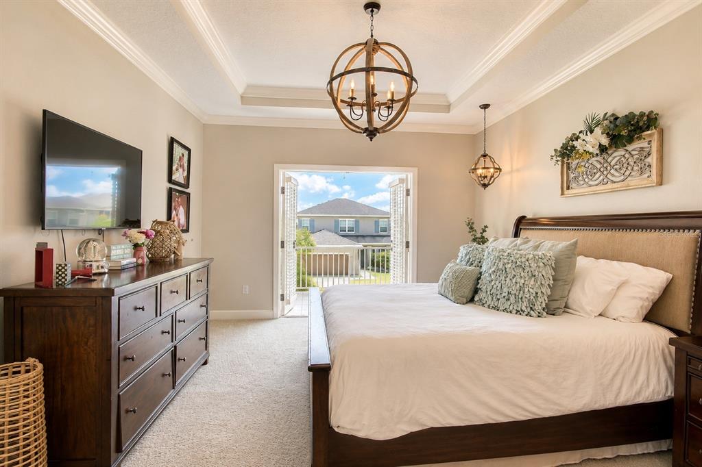 A bedroom features a wooden bed, a dresser, a chandelier, and a balcony with outdoor views — 10563 PIEDRA DR, PALMETTO, FL