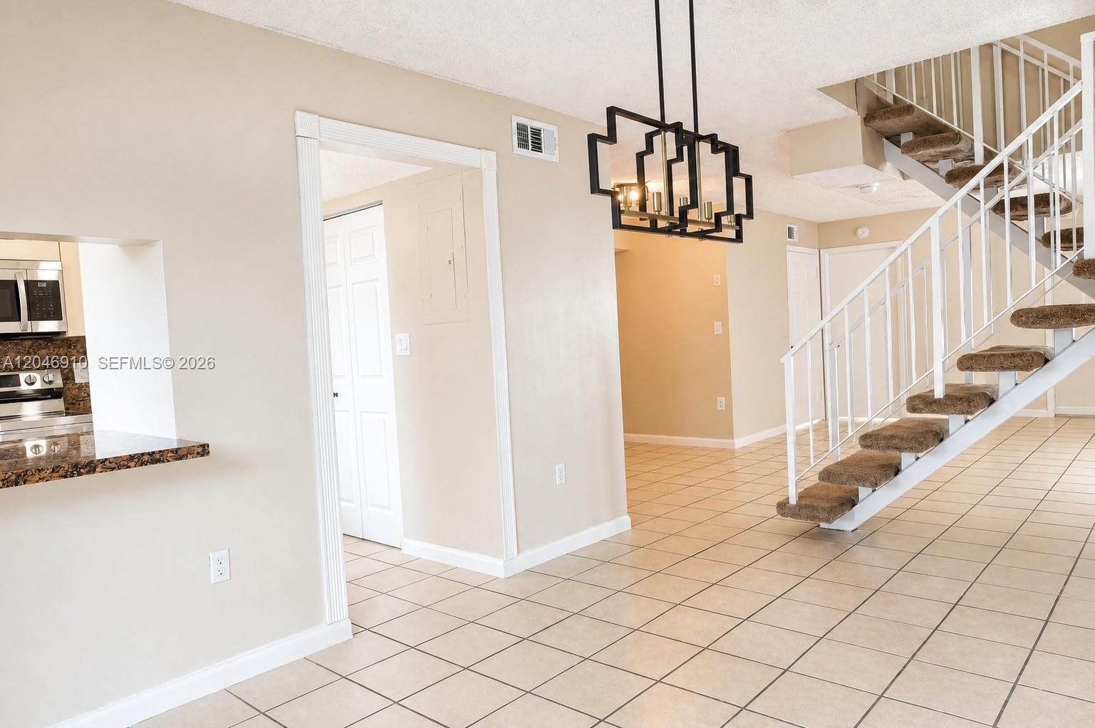 A tiled dining area features a modern chandelier, a staircase, and a kitchen pass-through — 1117 SW 104th Ct # 1117, Miami FL 33174, MIAMI, FL