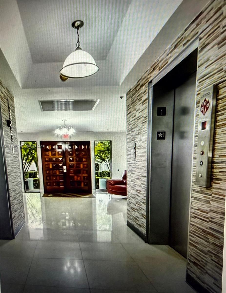 A building lobby features a stone-tiled wall, an elevator, and double wooden entry doors — 1825 W 44th Pl # 707, Hialeah FL 33012, HIALEAH, FL