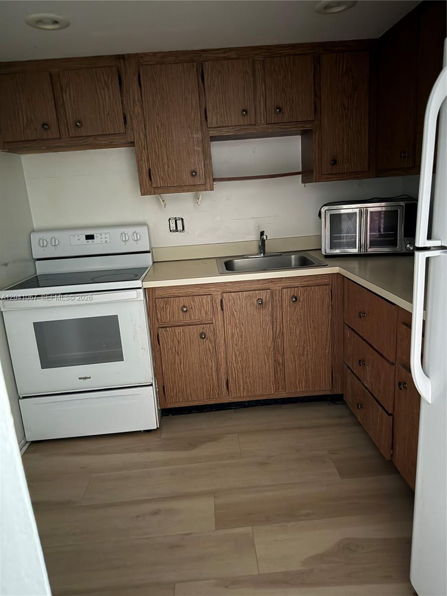 A kitchen features wood cabinets, a white stove, a stainless steel sink, and light flooring — 1825 W 44th Pl # 707, Hialeah FL 33012, HIALEAH, FL