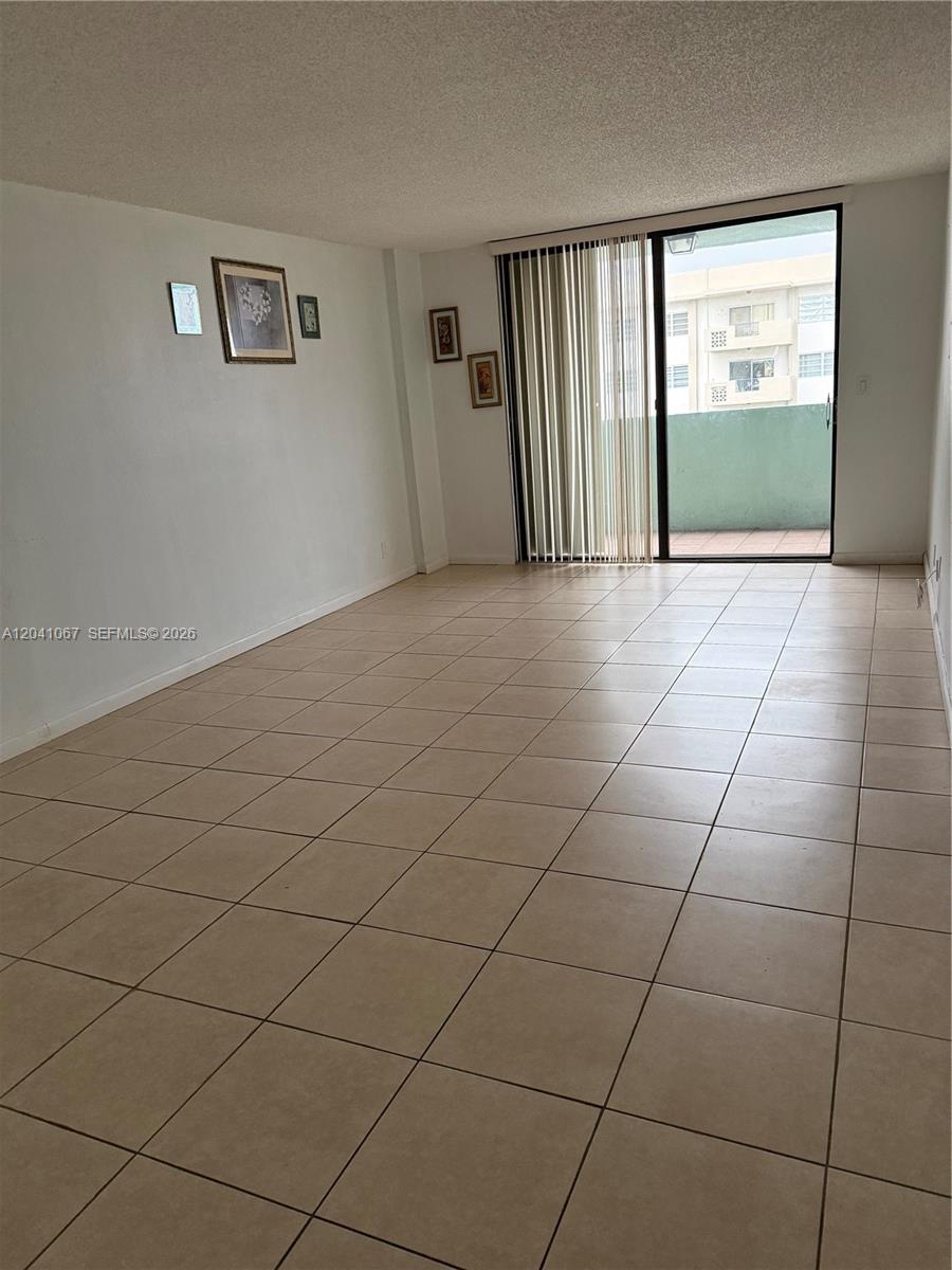 An empty room with beige tile flooring, white walls, and a sliding glass door — 1825 W 44th Pl # 707, Hialeah FL 33012, HIALEAH, FL