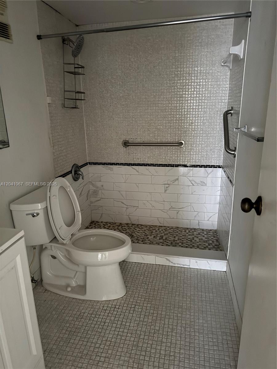 A bathroom features a toilet next to a walk-in shower with tiled walls and floors — 1825 W 44th Pl # 707, Hialeah FL 33012, HIALEAH, FL