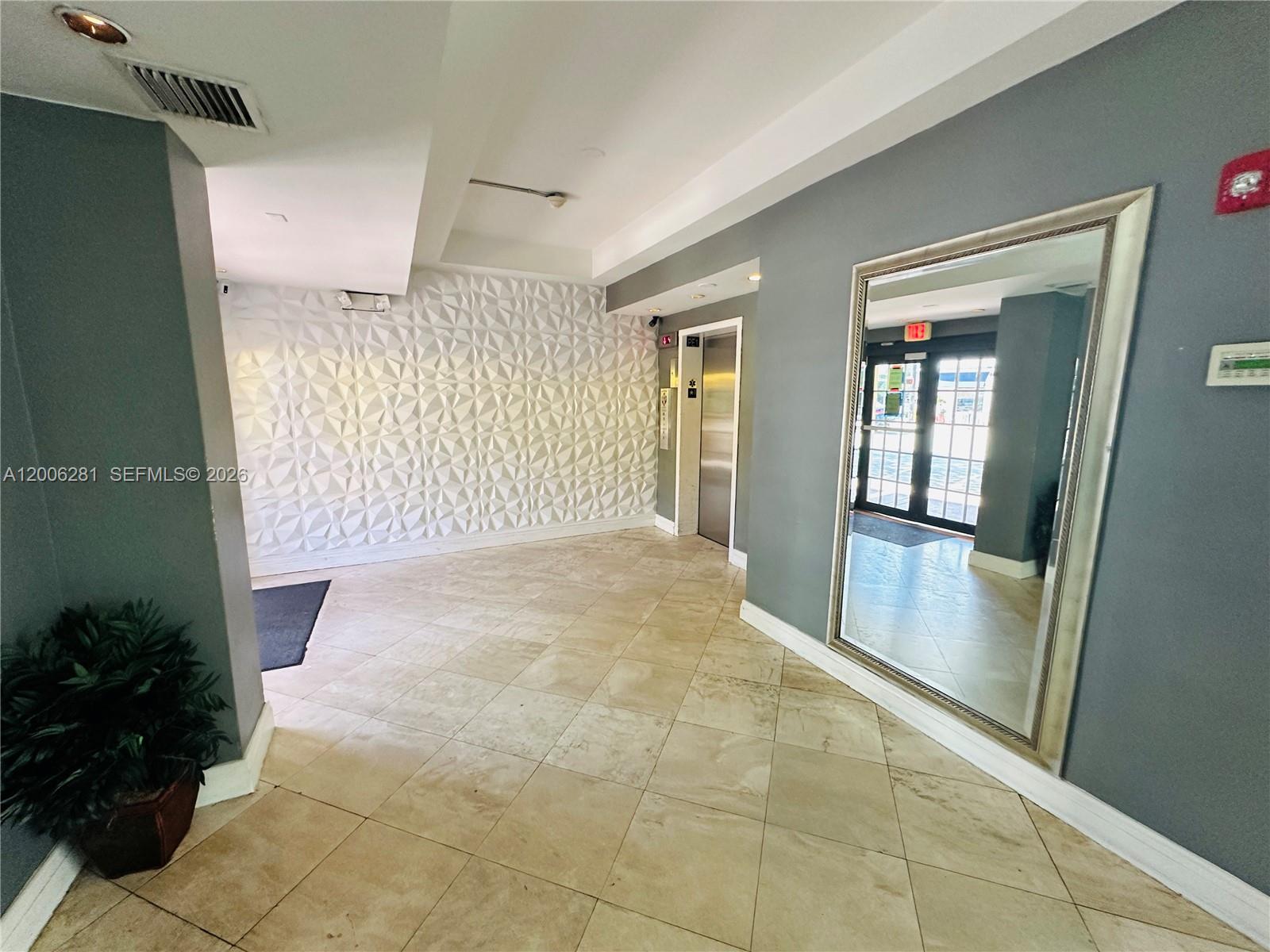 A lobby features a textured white wall, a large mirror, and an elevator — 710 Washington Ave # 321, Miami Beach FL 33139, MIAMI BEACH, FL
